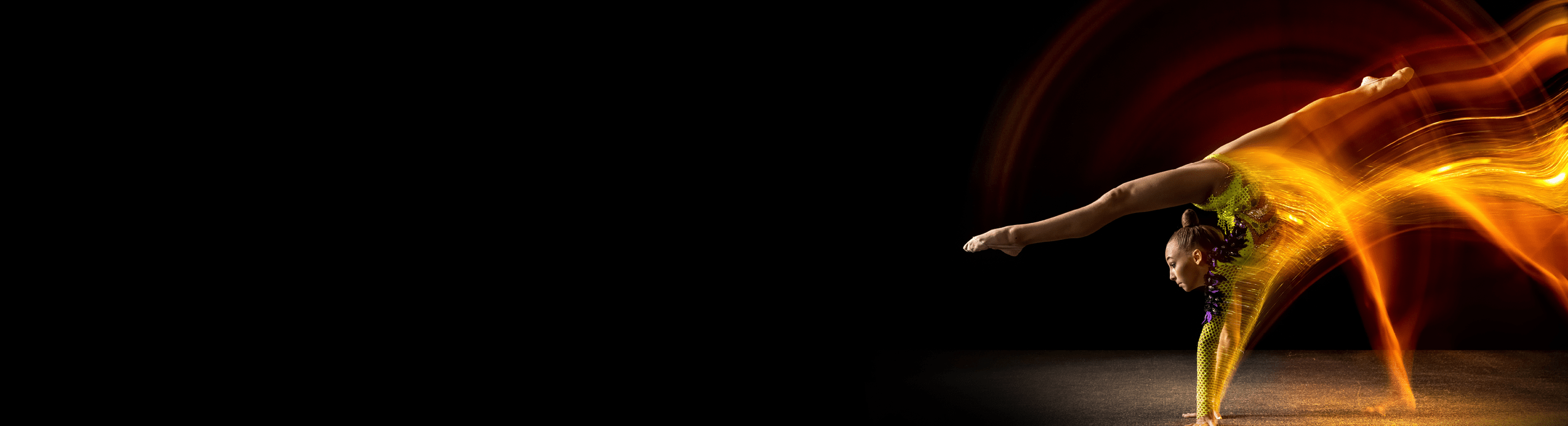 Portrait of young girl, rhythmic gymnastics artist in action isolated on dark studio background with mixed light. Concept of sport, action, aspiration, beauty. Handstand with legs in split position.