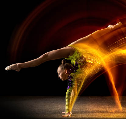 Portrait of young girl, rhythmic gymnastics artist in action isolated on dark studio background with mixed light. Concept of sport, action, aspiration, beauty. Handstand with legs in split position.