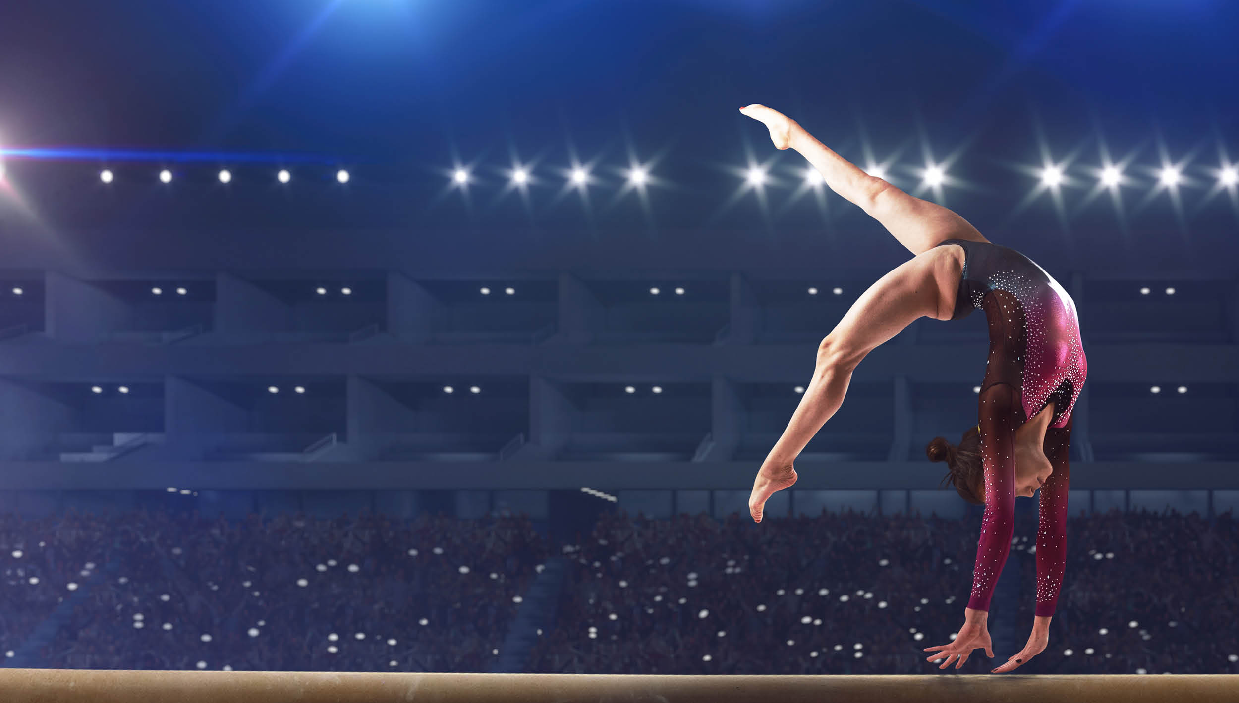 Female gymnast doing a complicated trick on gymnastics balance beam in a professional arena.